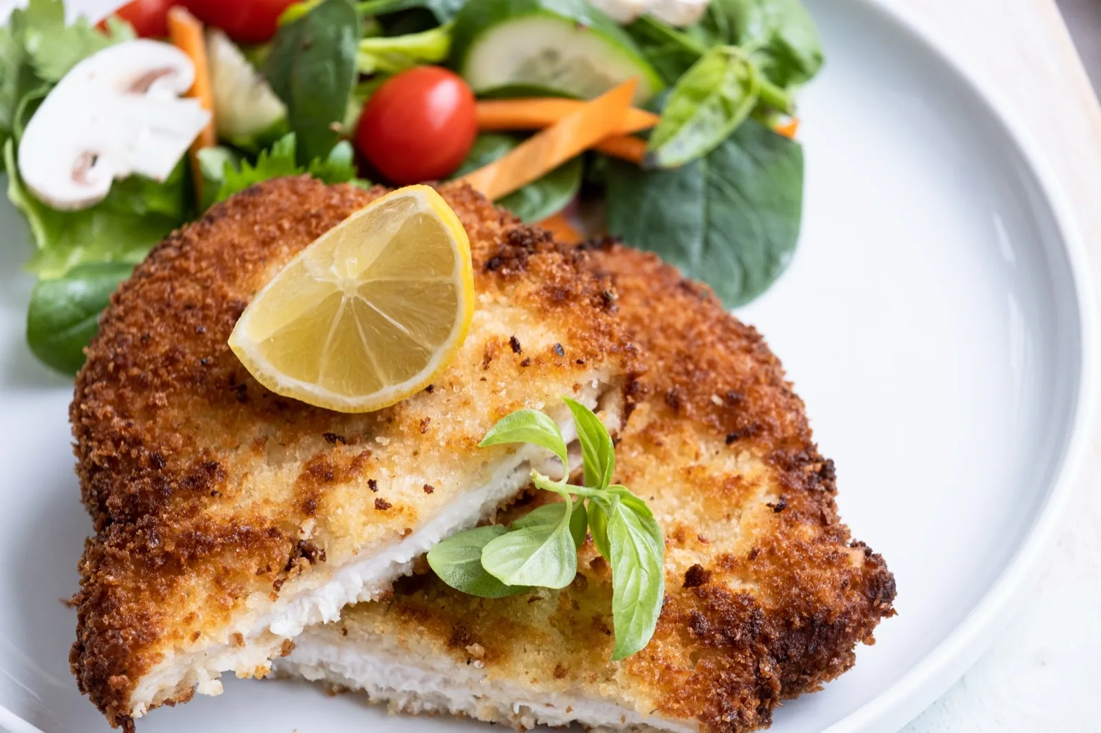 Chicken schnitzel cut open to show the coarse golden crumb and lemon