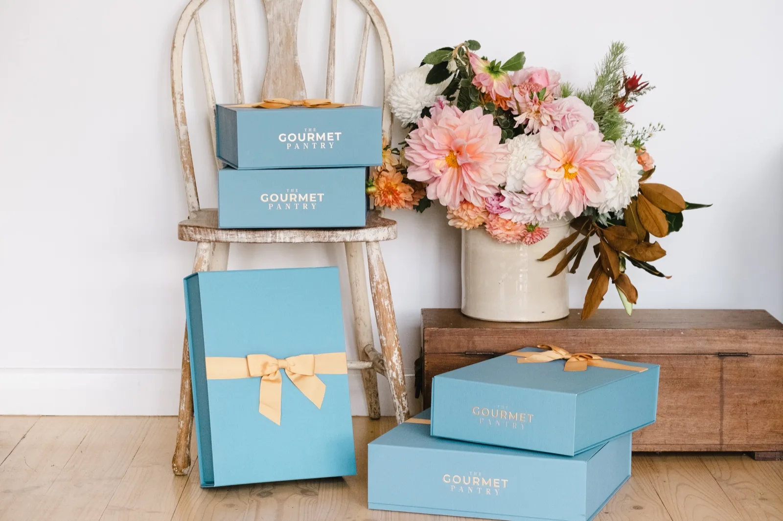 The Gourmet Pantry hampers in French Blue boxes tied with gold ribbon, grouped by size on a timber floor