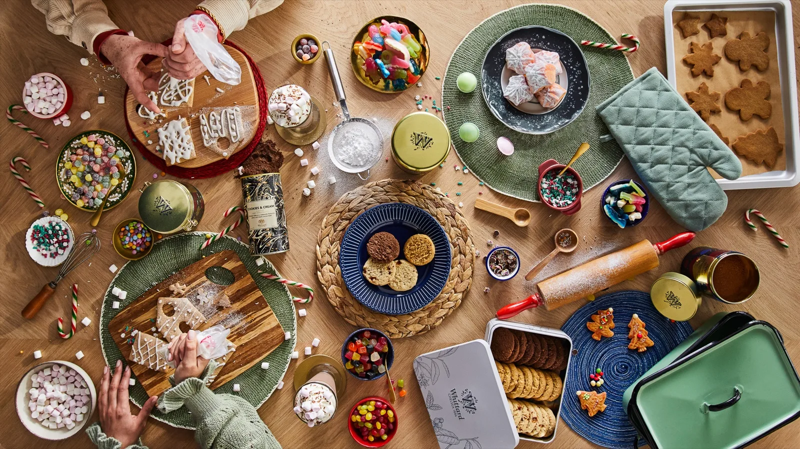 Christmas table of gingerbread shapes, jelly lollies, marshmallows, plain biscuits and hot chocolate