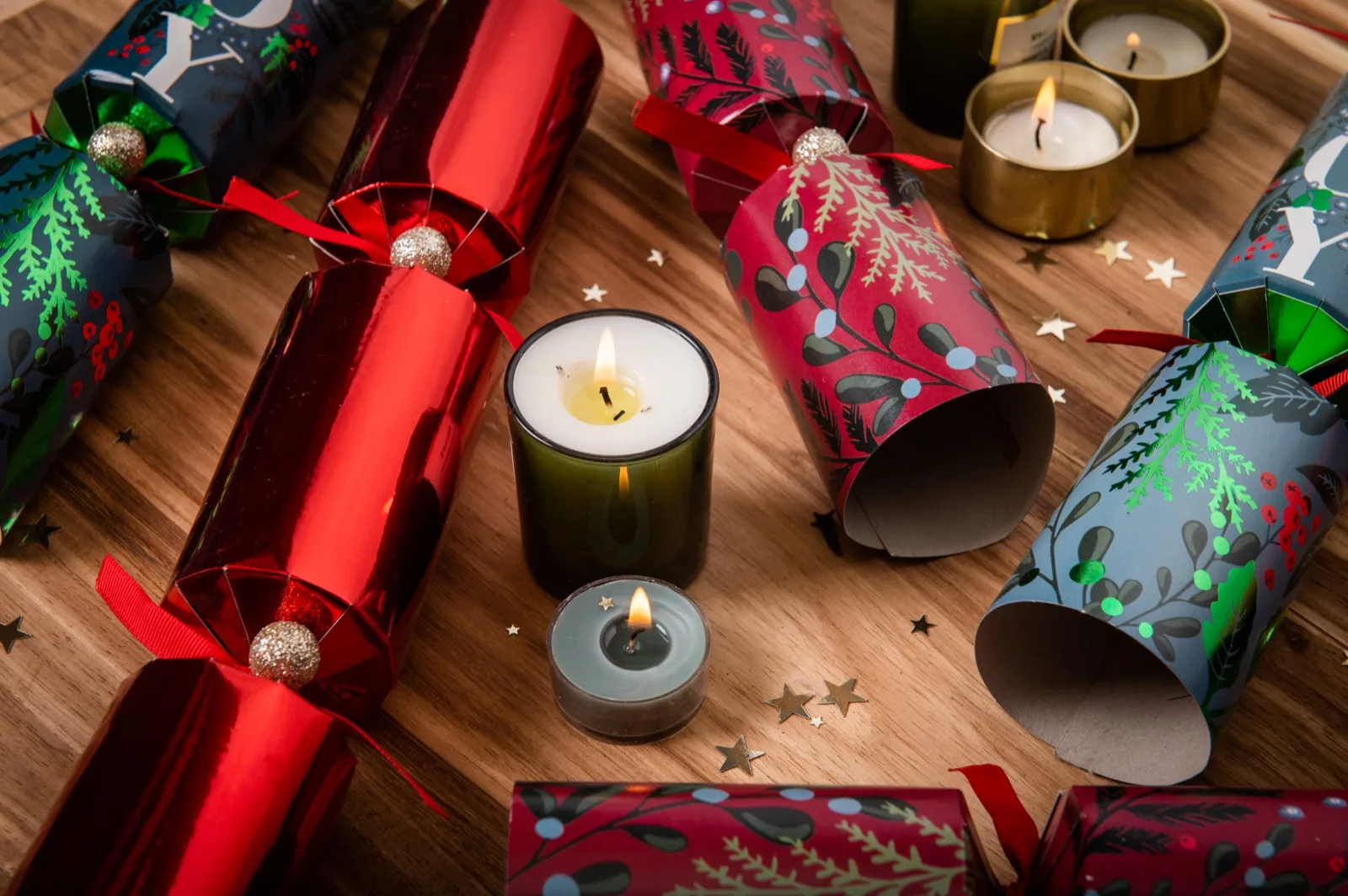 Red foil, blue Joy and mistletoe print Christmas bon bons laid on a timber table with lit candles