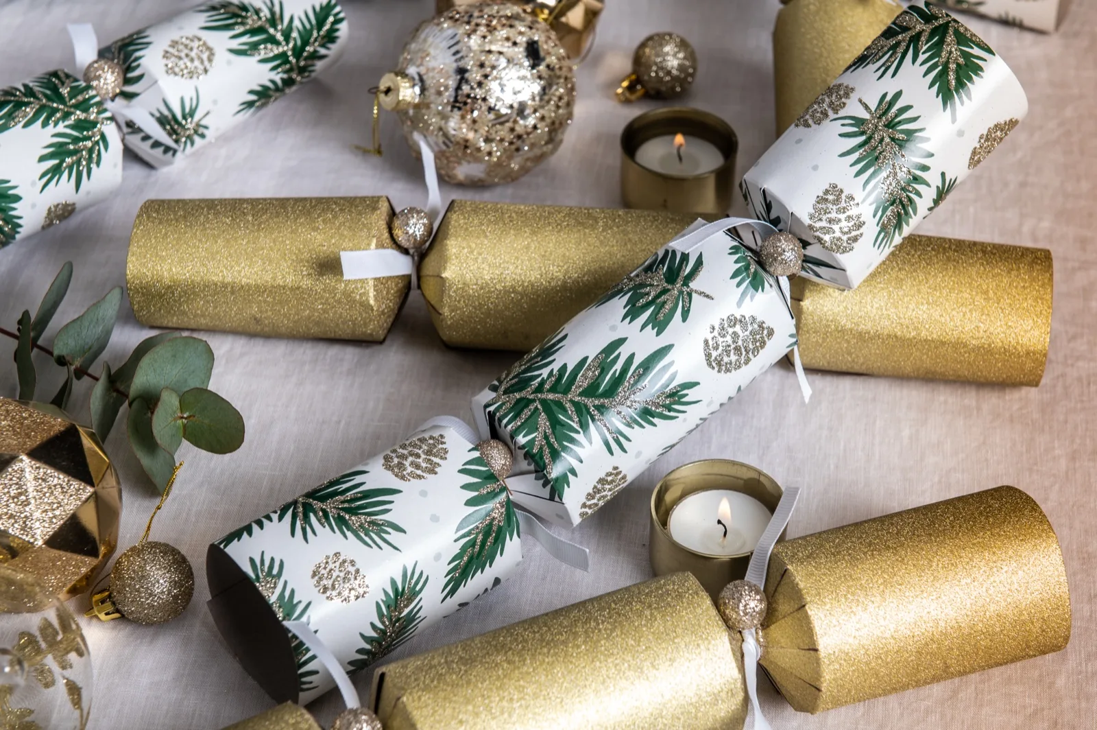 Gold glitter and fir print Christmas bon bons on a linen tablecloth with tealights and eucalyptus