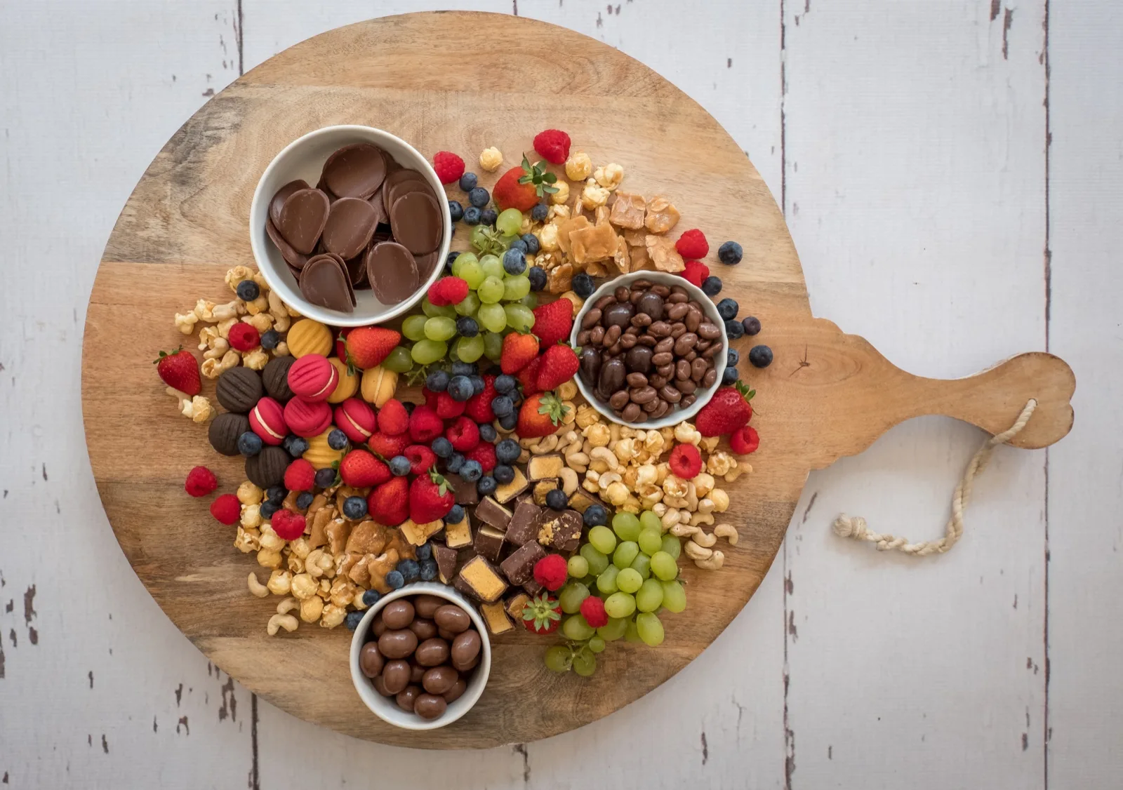 Cold Christmas dessert board with chocolate buttons, macarons, caramel popcorn, strawberries and grapes