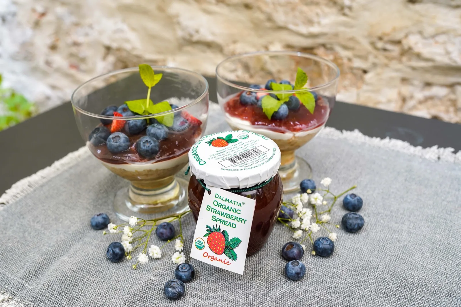 Two layered berry desserts in glass coupes topped with blueberries, strawberries and mint, served outdoors