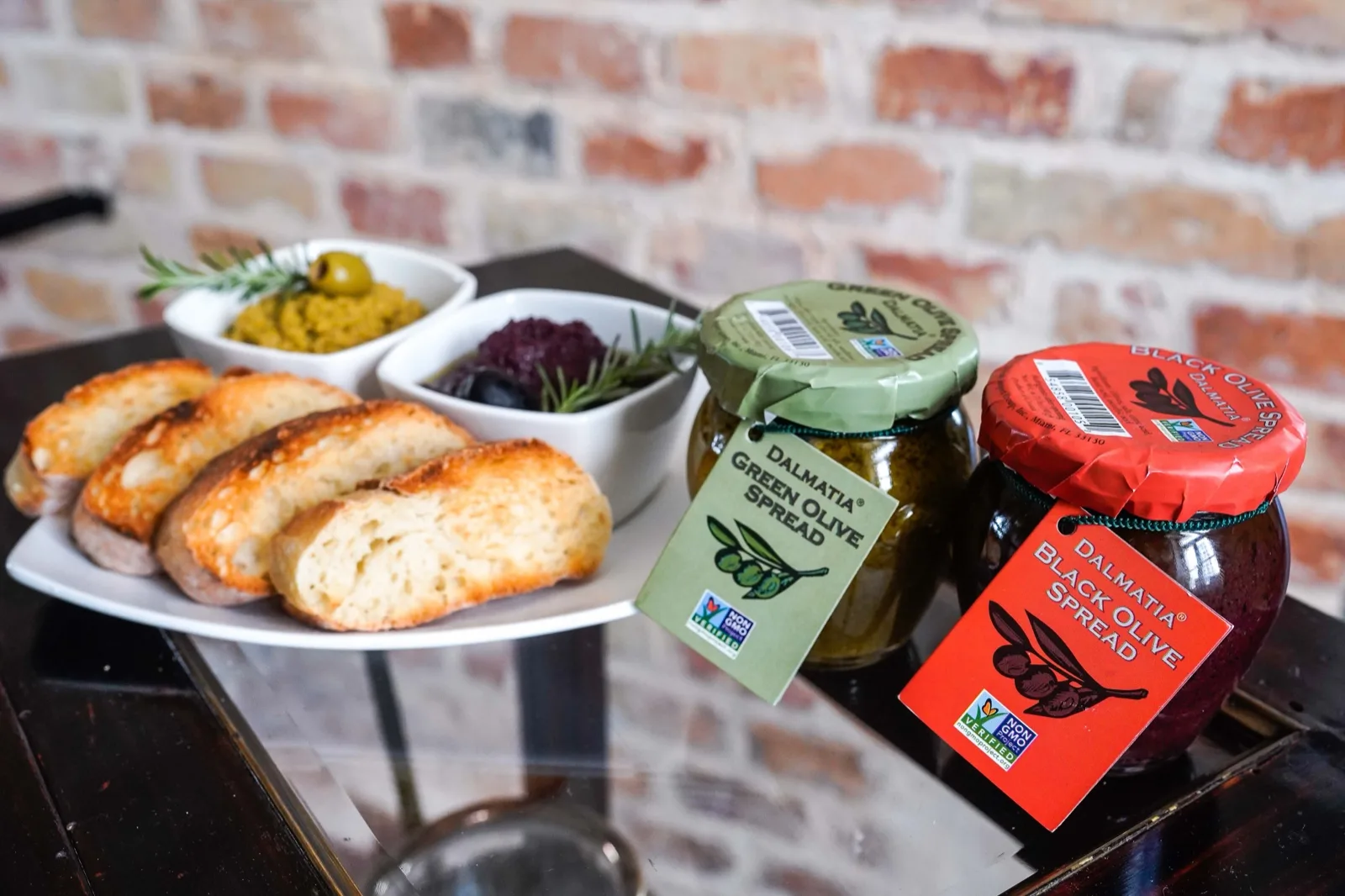 Toasted bread with small bowls of green olive and black olive spread beside two Dalmatia jars