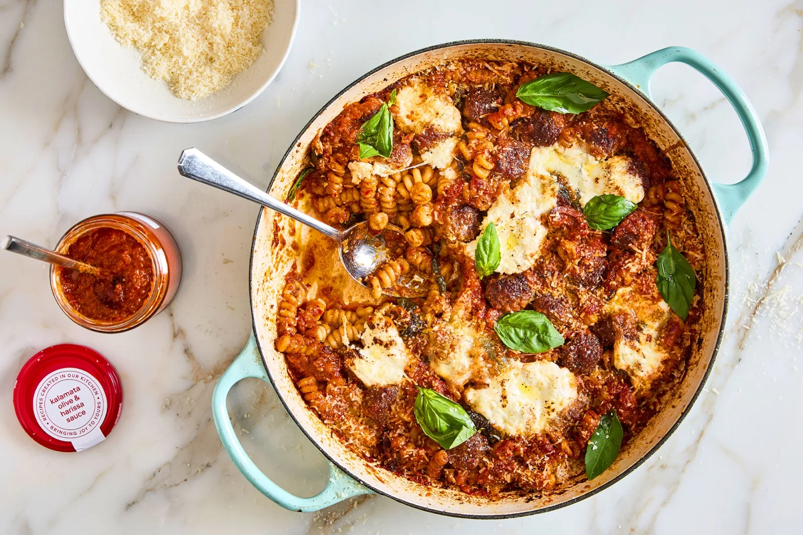 One pan pasta bake with meatballs, mozzarella and basil beside an open jar of kalamata olive and harissa sauce