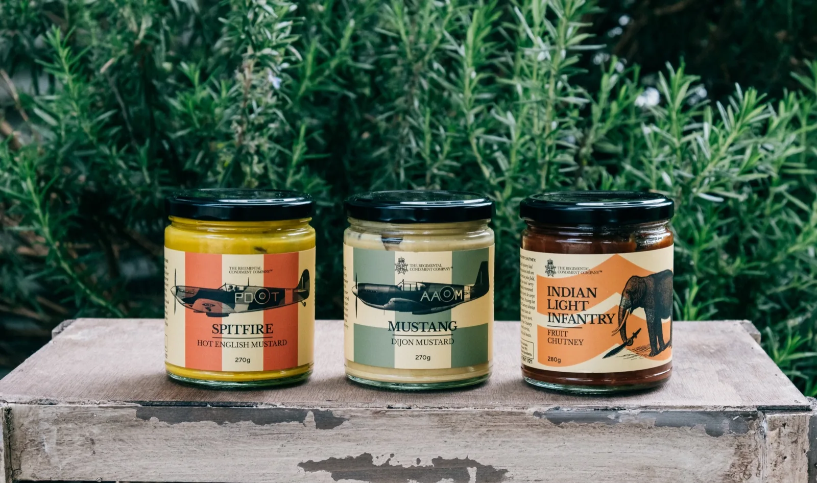 Jars of hot English mustard, Dijon mustard and fruit chutney lined up on a weathered timber bench