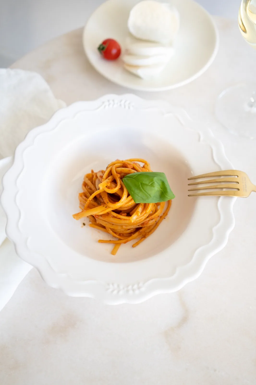 Pasta coated in red sun dried tomato pesto topped with a basil leaf, with sliced mozzarell
