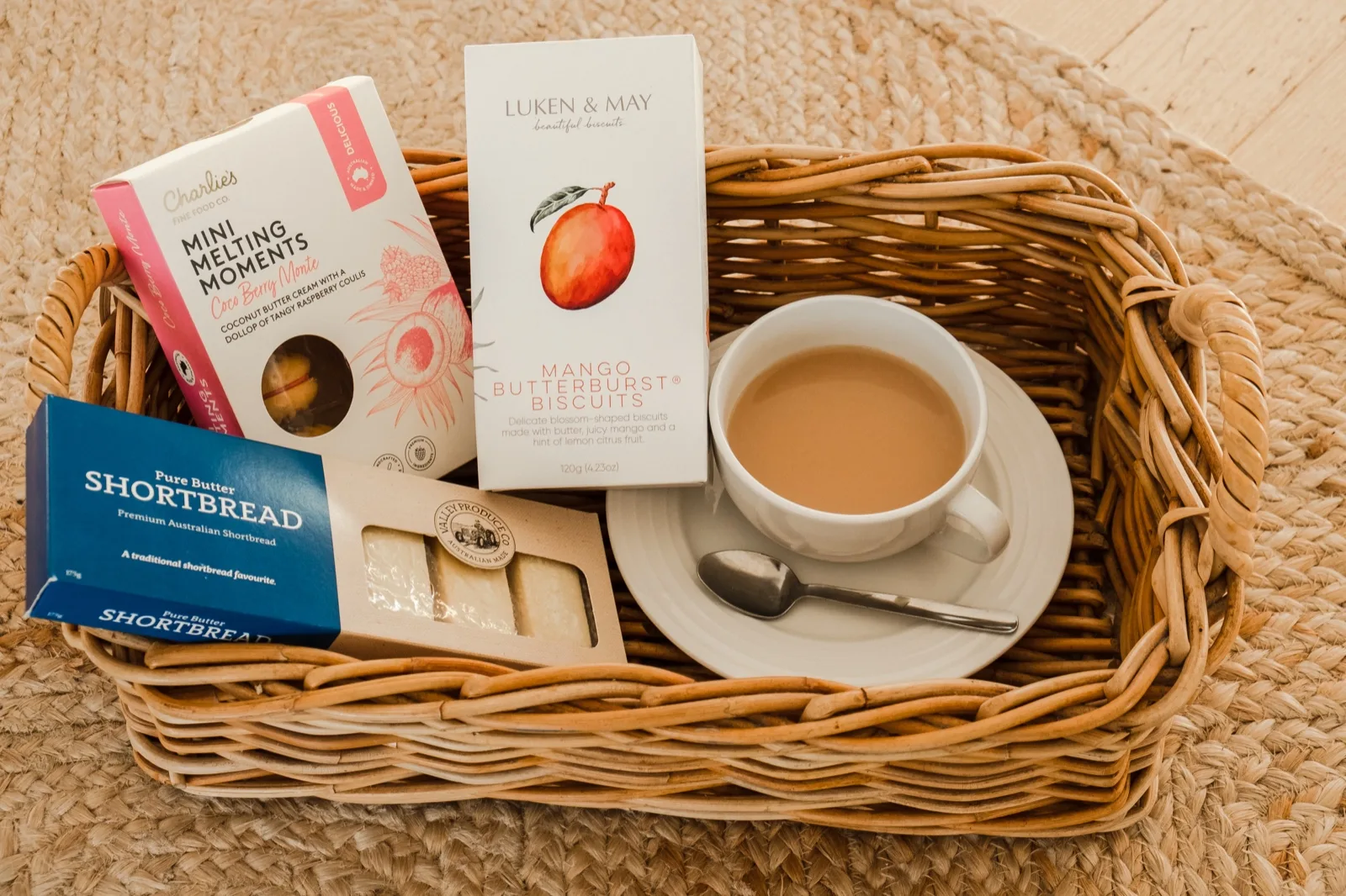 Wicker gift basket of pure butter shortbread, mango biscuits and melting moments beside a cup of tea