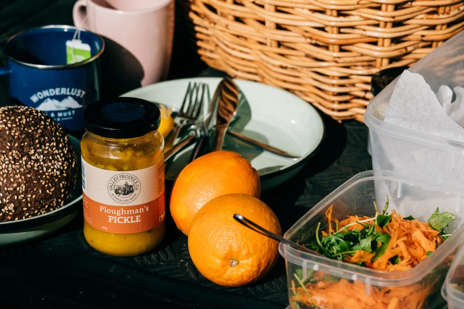 Sealed containers of carrot salad packed with a seeded roll, oranges, camp mugs and a jar of Ploughman's Pickl