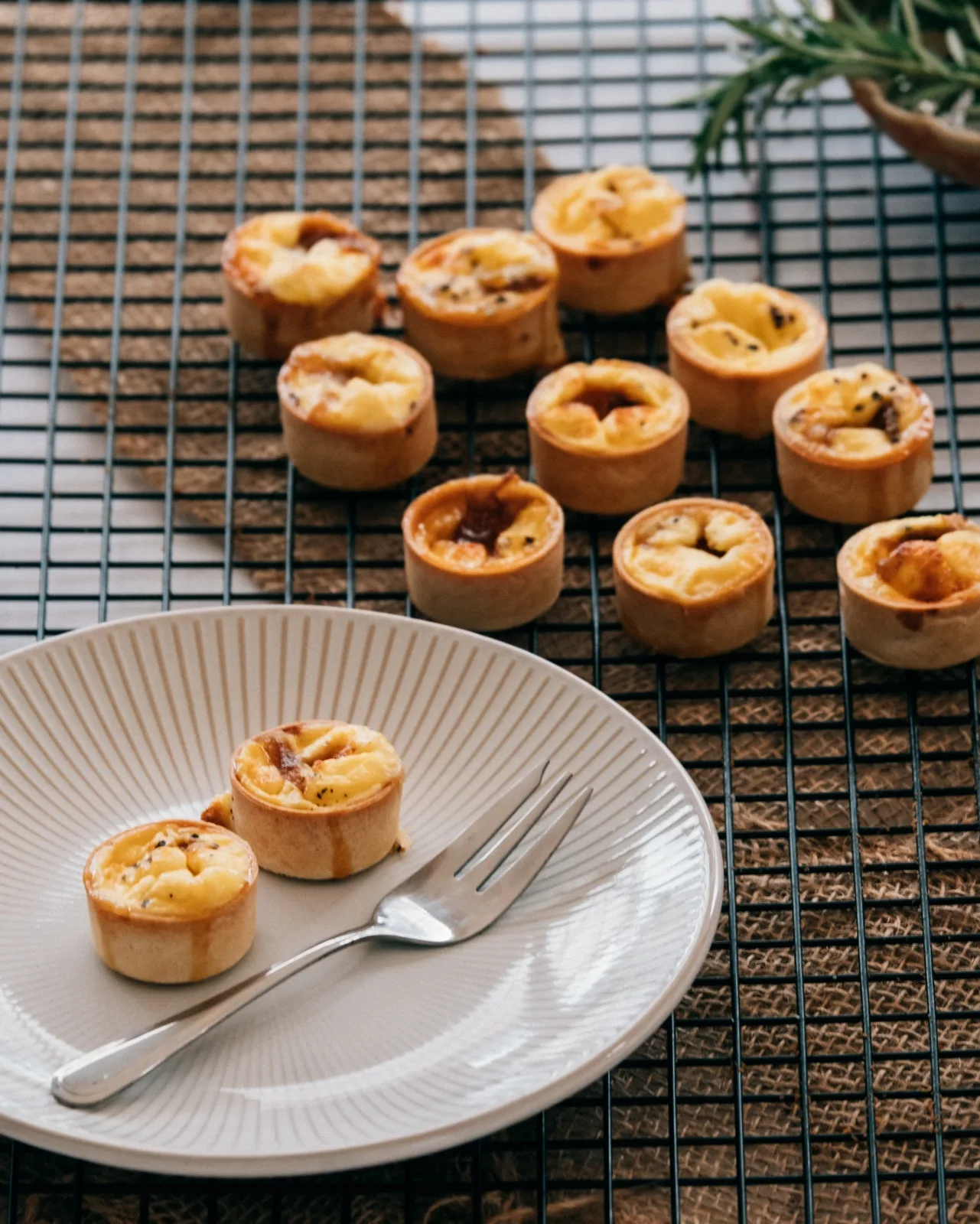 Filled mini savoury tart cases cooling on a wire rack with two plated, showing the crisp pastry wall