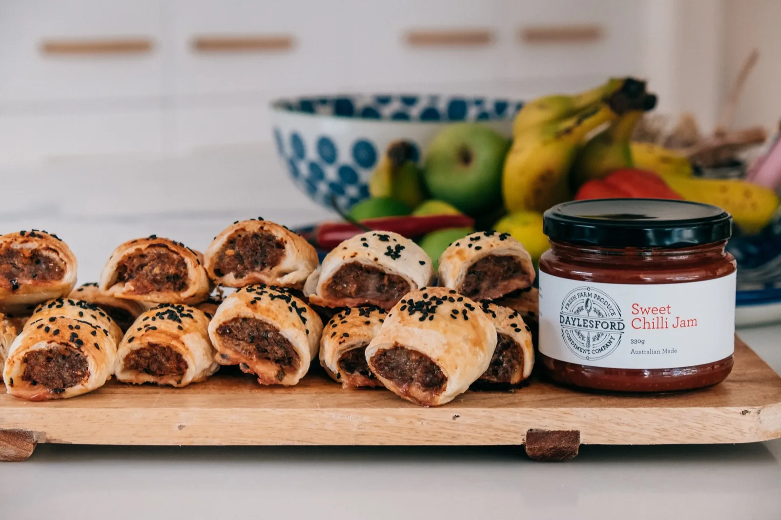Daylesford Condiment Company Sweet Chilli Jam jar beside a board of mini sausage rolls in a bright kitchen