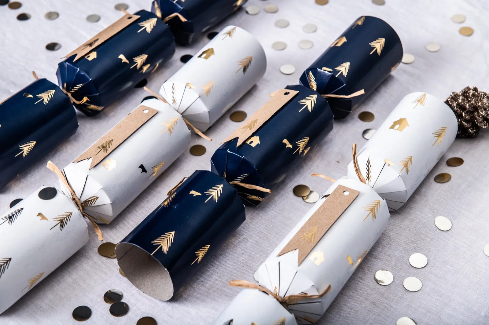 Navy and white Christmas crackers tied with raffia and kraft tags, one showing its open cardboard tube