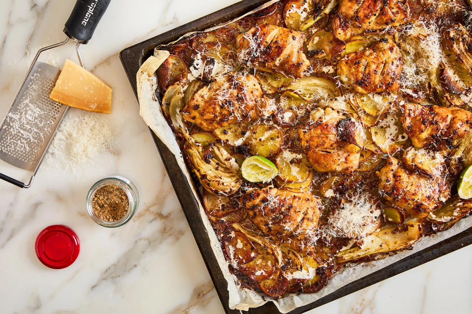 Roast chicken thighs on a tray of sliced potato and fennel with lime wedges and a scatter