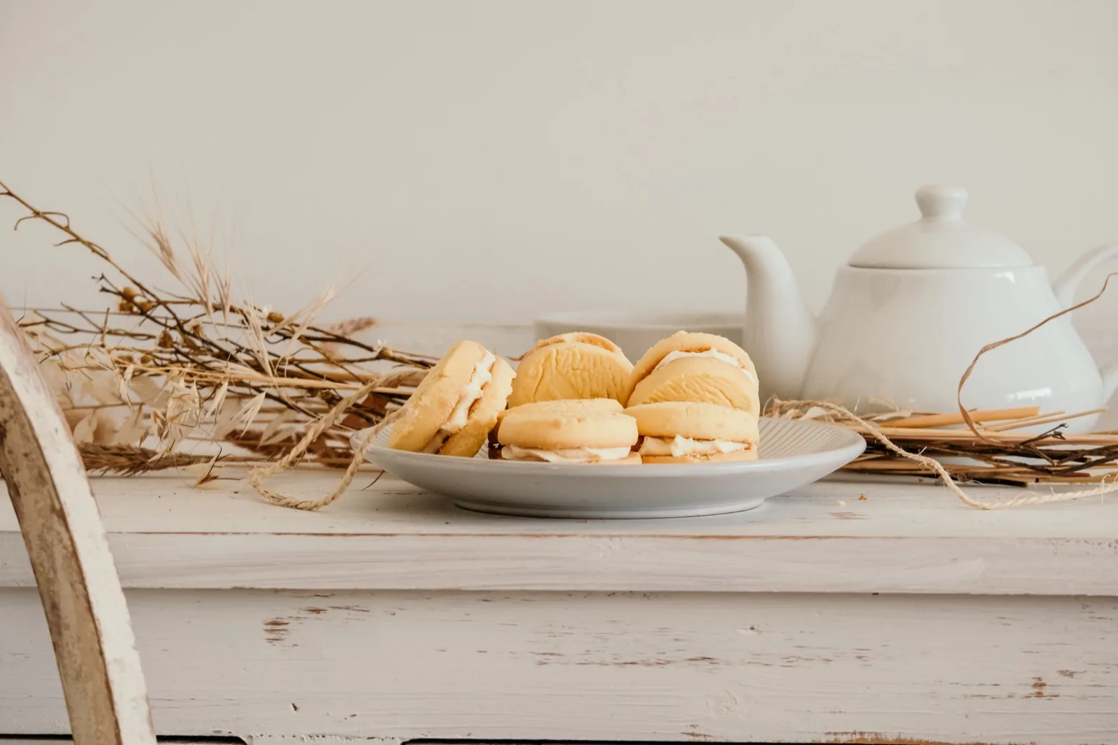 Cream filled melting moments on a plate beside a white teapot on a painted kitchen bench
