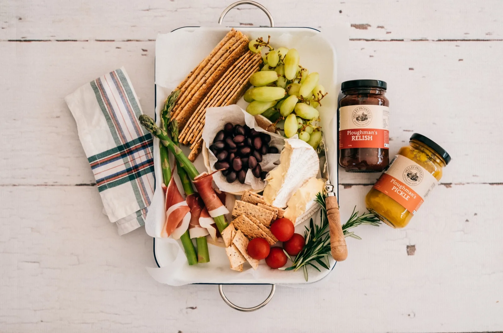 Ploughman's plate of cured meat, brie, olives and crackers beside jars of Ploughman's relish and pickle