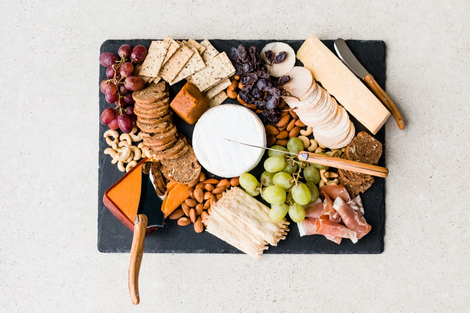 Grazing board of crackers, brie, cheddar, quince paste, almonds, cashews and grapes on a slate platter