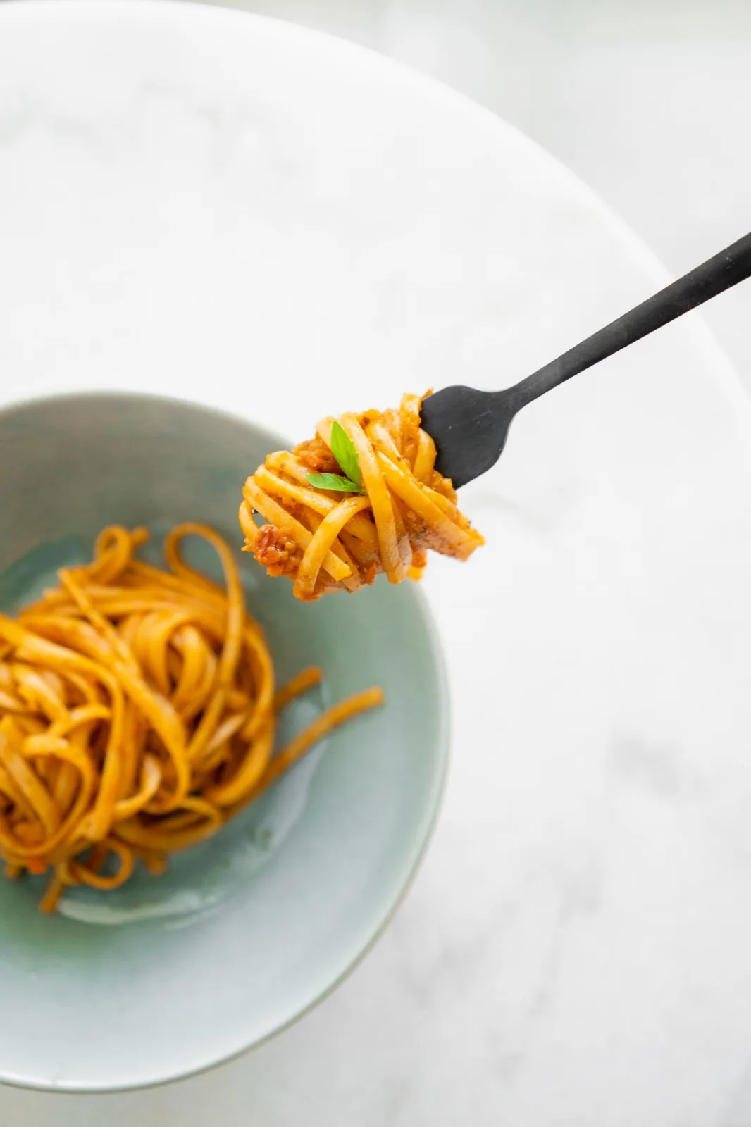 Long pasta lifted on a fork above a bowl, each strand coated in a glossy red tomato sauce