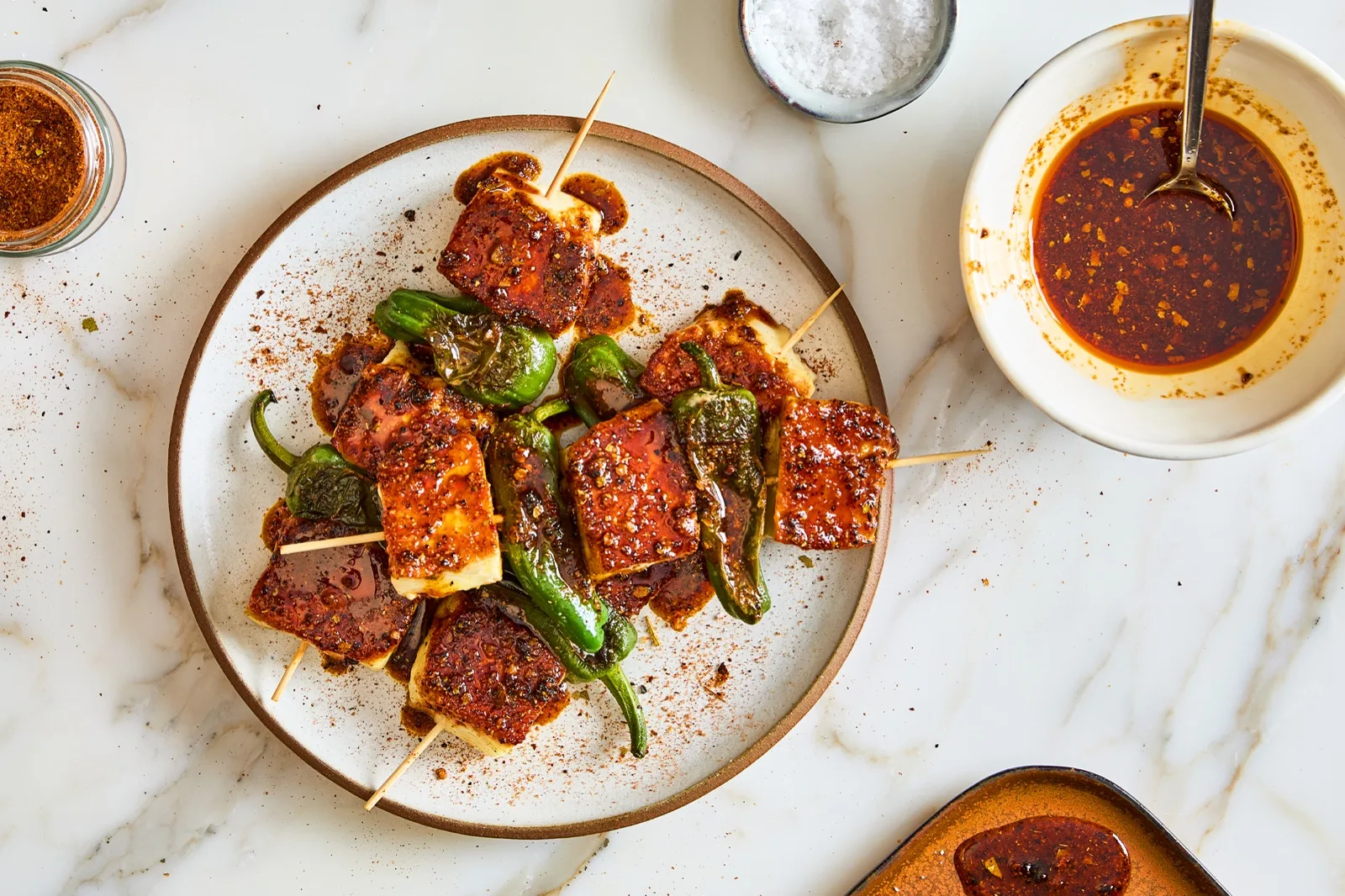 Grilled halloumi and Padron pepper skewers in a dark smokey honey glaze, with the glaze in a bowl beside