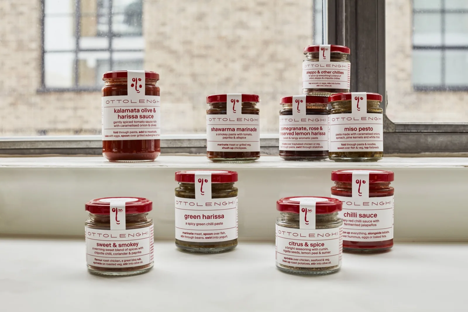 Ottolenghi jars including shawarma marinade, miso pesto and harissa lined up on a kitchen windowsill