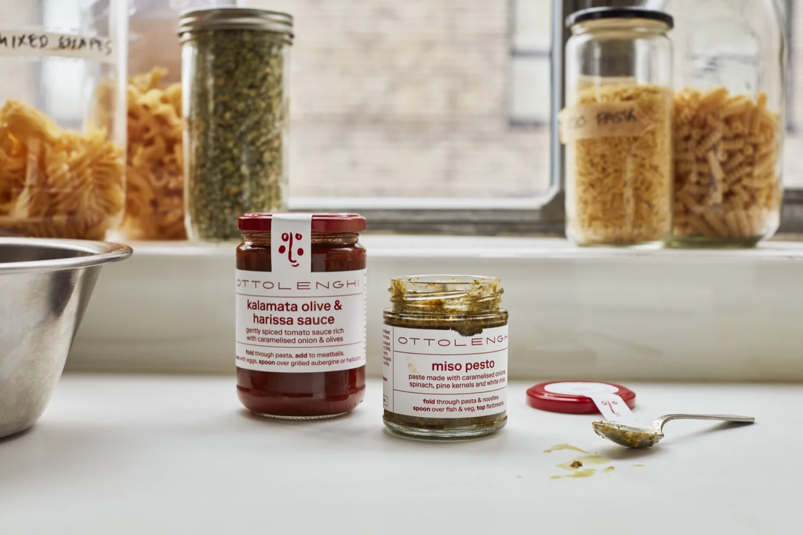 Ottolenghi kalamata olive and harissa sauce and miso pesto jars on a kitchen sill beside j