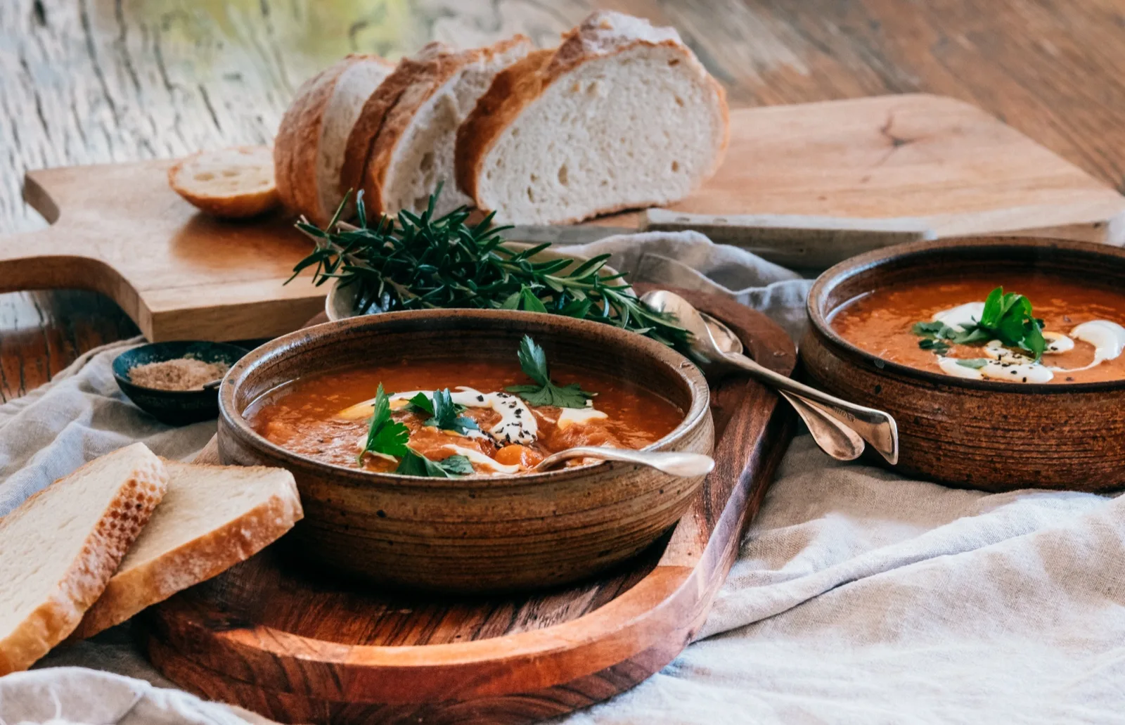 Two rustic bowls of spiced orange soup swirled with yoghurt and black seeds, sliced bread 