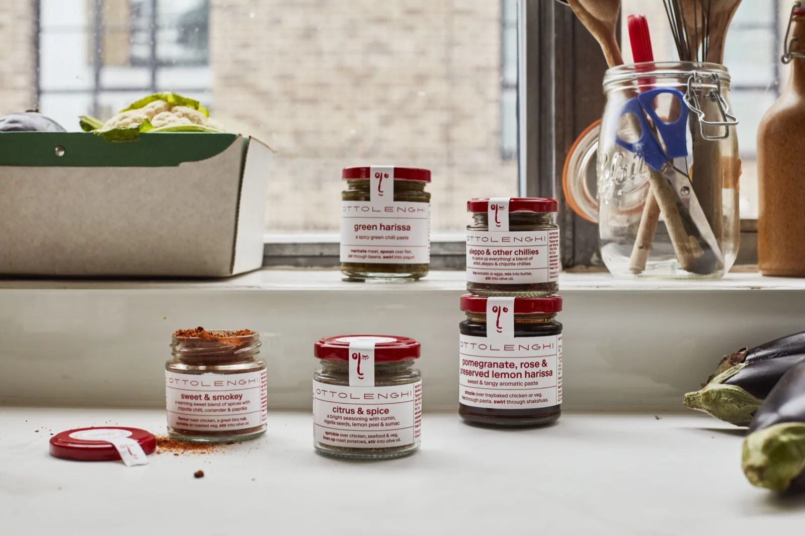 Ottolenghi harissa and spice jars on a kitchen windowsill beside two whole aubergines and 