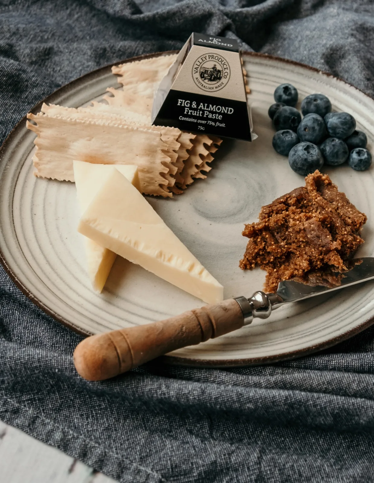 Valley Produce Co fig and almond fruit paste on a knife with cheese, lavosh and blueberrie