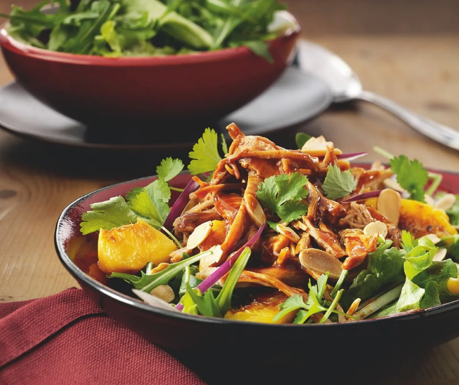 Summer salad of shredded meat, orange segments, coriander and flaked almonds with a bowl of leaves behind