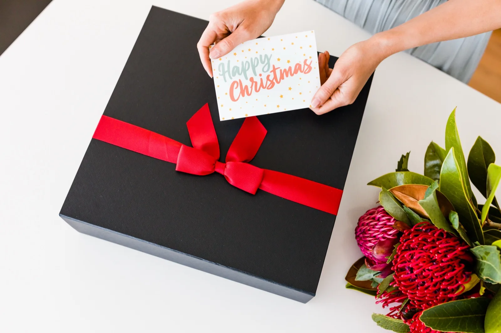 Hands setting a Happy Christmas card on a closed black hamper box tied with red ribbon