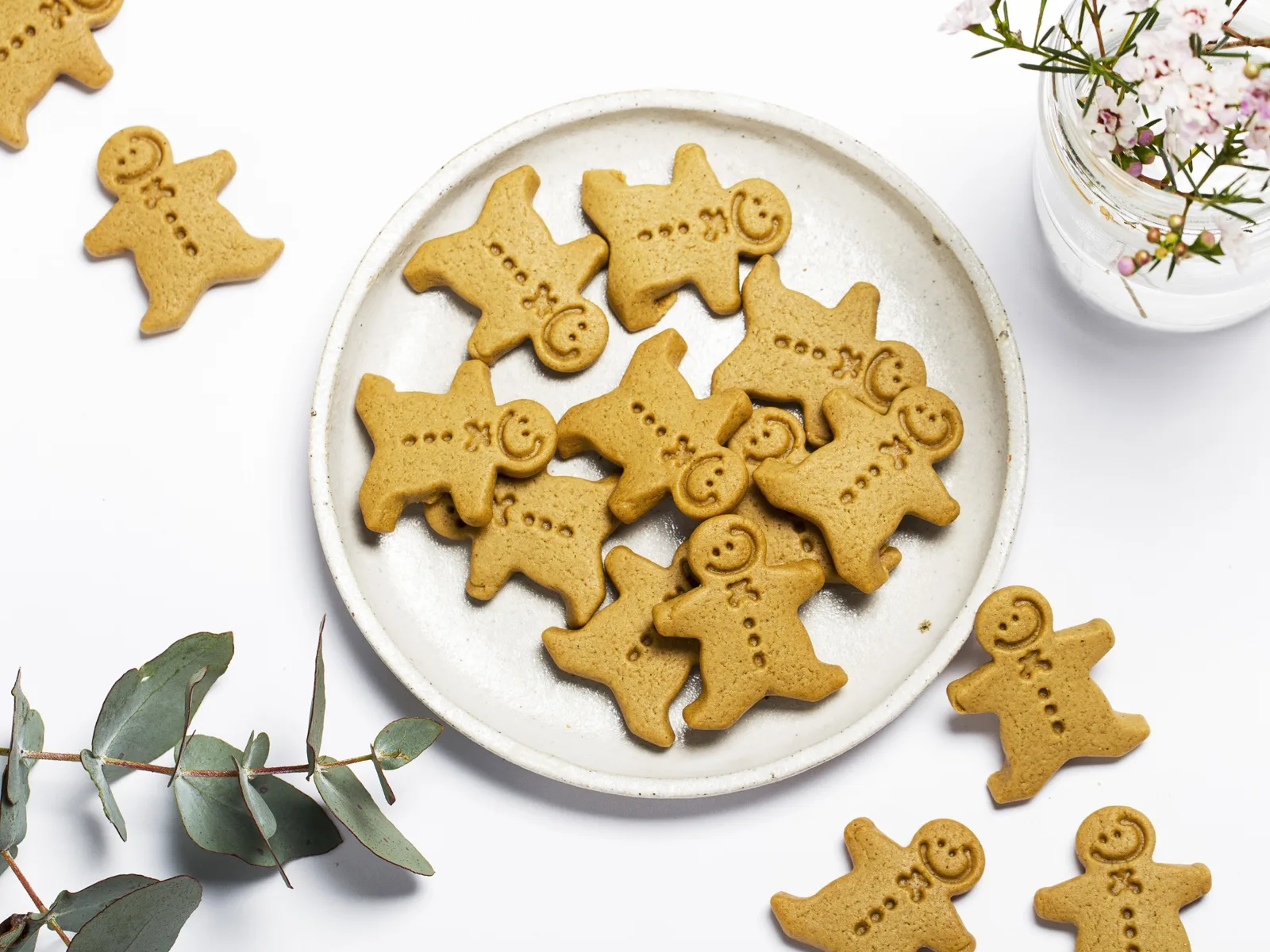 Gingerbread biscuits on a speckled ceramic plate with gum leaves and waxflower on a white 