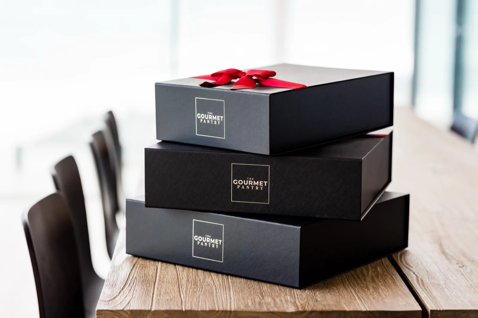 Three The Gourmet Pantry hamper boxes in three sizes stacked on a boardroom table in an office