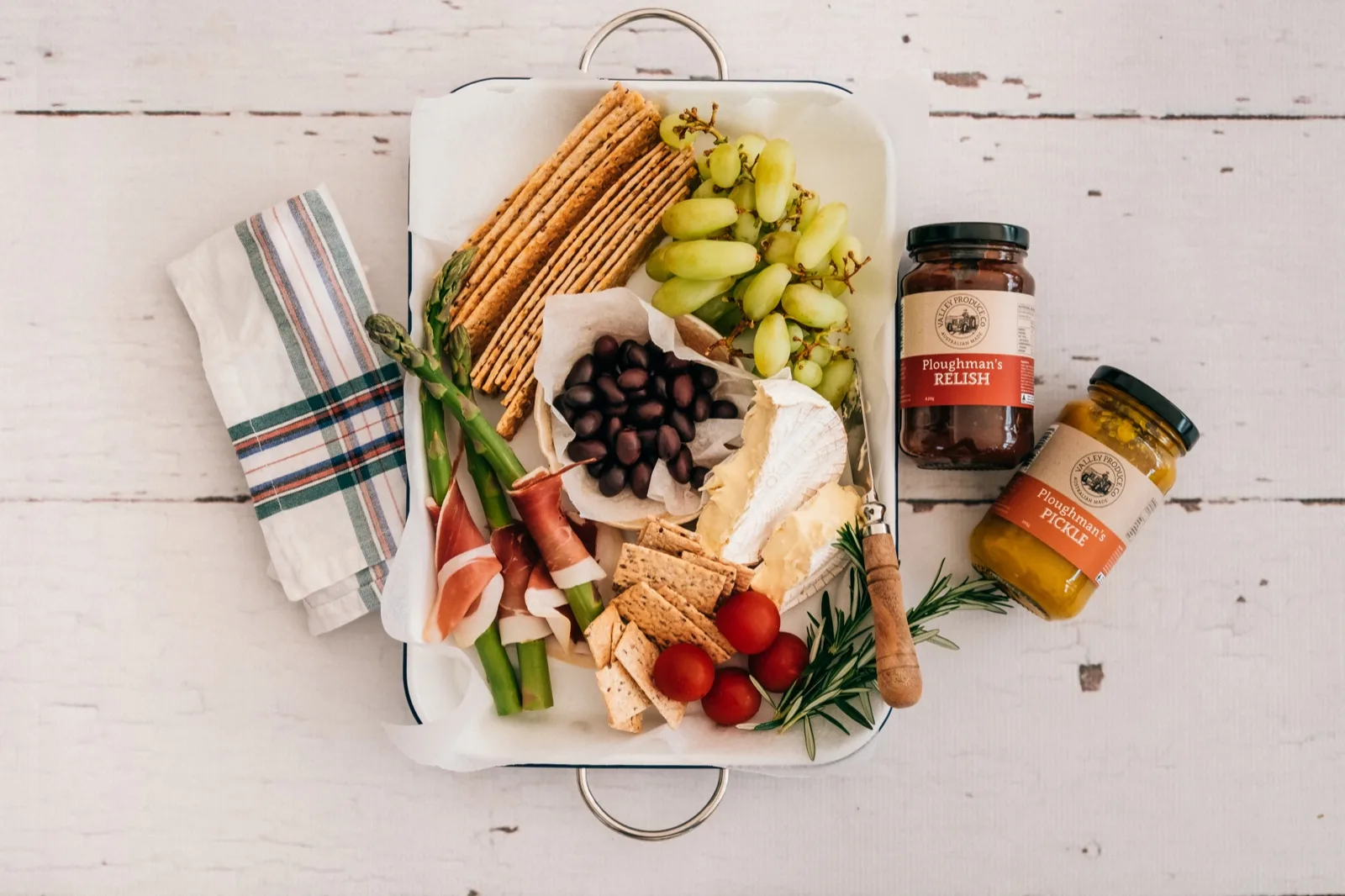 Brie, seeded crackers, olives and prosciutto on an enamel tray beside Valley Produce Co re